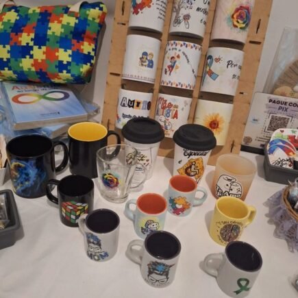Mesa expositora com diversas canecas, botons, livros, necessaire com desenhos e frases do TEA.
