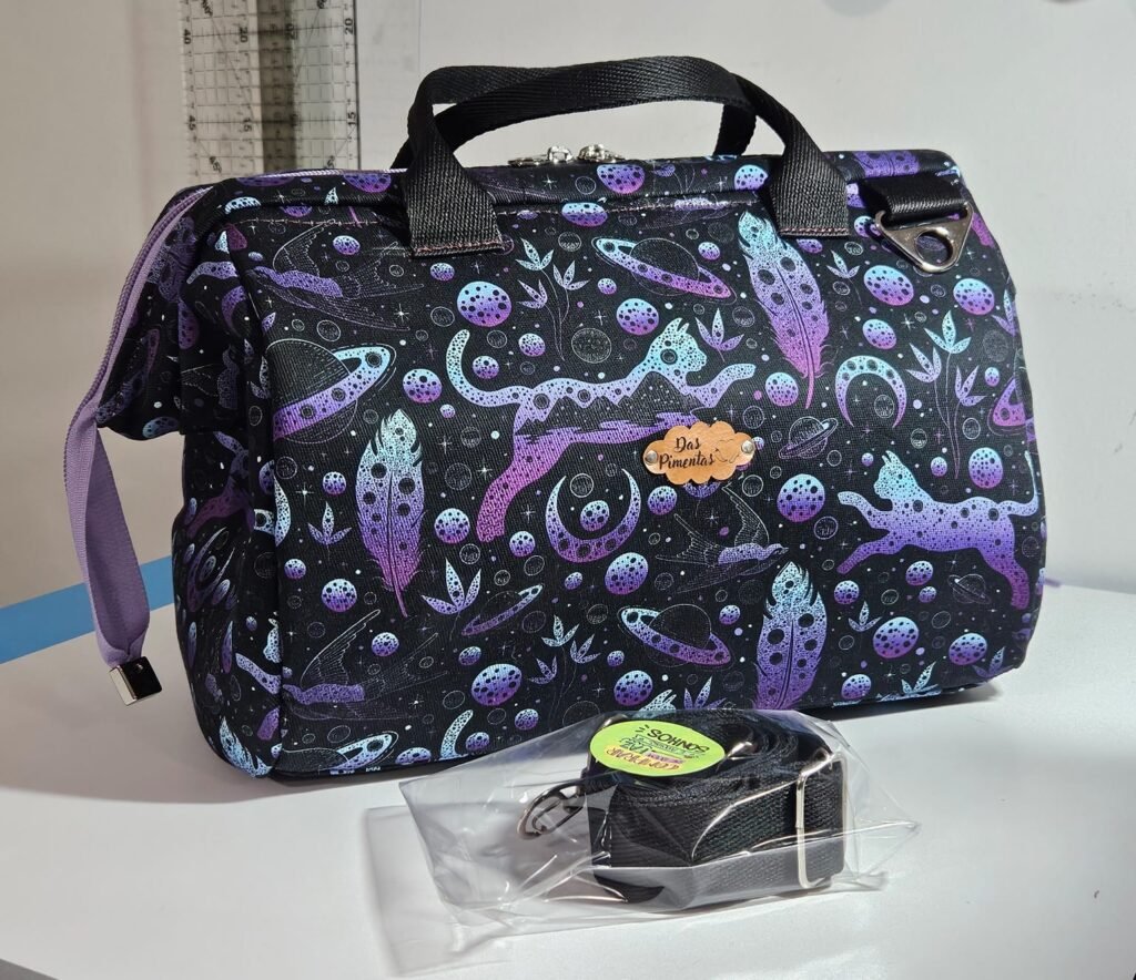 Bolsa de tecido com fundo preto e diversas estampas de folhas, naves espaciais e outros detalhes com um porta-moeda na frente da bolsa.